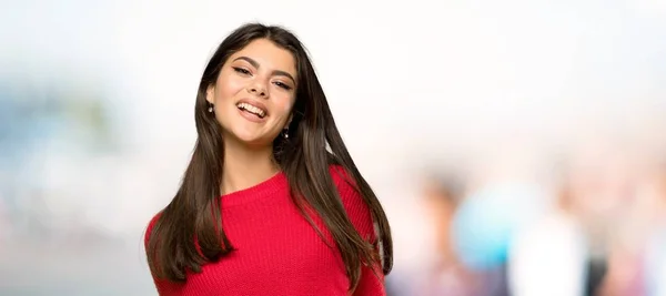 屋外で正面を見て笑っている赤いセーターを持つティーンエイジャーの女の子 — ストック写真