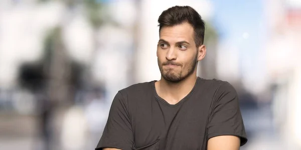 Man with black shirt making doubts gesture while lifting the shoulders at outdoors