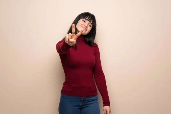 Young woman with red turtleneck smiling and showing victory sign