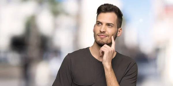 Man with black shirt thinking an idea while looking up at outdoors