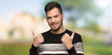 Yakışıklı adam veren bir thumbs yukarı jest ve gülümsüyor açık havada