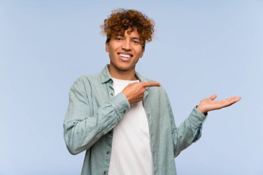Bir reklam eklemek için avuç üzerinde copyspace hayali tutan izole mavi duvar üzerinde Genç Afrikalı Amerikalı adam