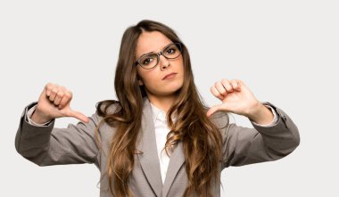 İzole gri arka planda her iki eliyle başparmak aşağı gösteren iş kadını