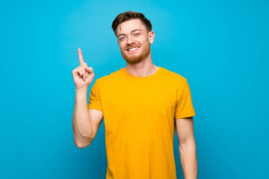 Mavi duvar üzerinde Redhead adam gösteren ve en iyi işareti bir parmak kaldırma