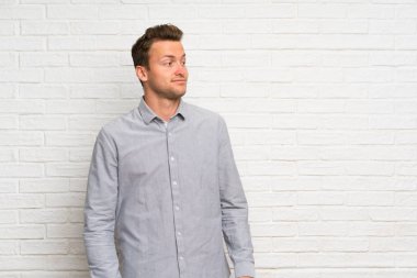 Sarışın adam üzerinde beyaz tuğla duvar yapma şüpheler jest görünümlü yan