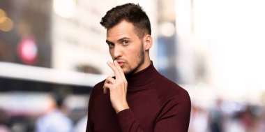 Şehirde ağzına parmak koyarak sessizlik jest bir işareti gösteren balıkçı yaka kazak ile adam