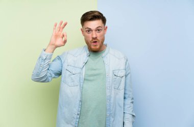 Renkli arka plan üzerinde Redhead adam şaşırttı ve ok işareti gösteren