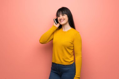 Pembe duvarda sarı kazaklı bir kadın cep telefonuyla sohbet ediyor.