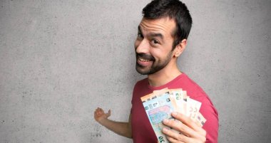 Adam geri işaret ve dokulu duvar üzerinde bir ürün sunan bir sürü para alarak