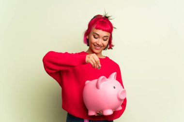 Kırmızı kazaklı genç bir kadın kumbarayı alıyor ve mutlu çünkü kumbara dolu.