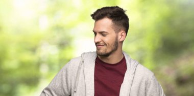 Sweatshirt ile kalça silah poz ve bir parkta gülümseyen adam