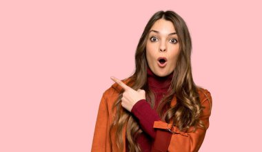 Ceket ile genç kadın sürpriz ve izole pembe arka plan üzerinde yan işaret