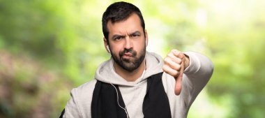 Bir parkta negatif ifade ile başparmak aşağı işareti gösteren spor adam