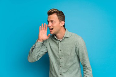 İzole mavi duvar üzerinde sarışın adam ağız geniş lateral açık bağırarak