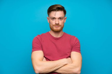 Kolları çapraz tutan izole mavi duvardaki kızıl saçlı adam