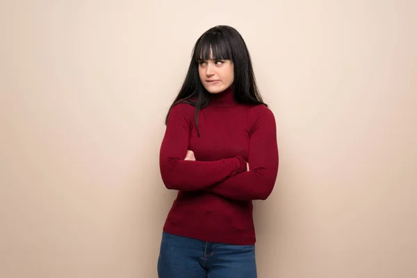 Young woman with red turtleneck with confuse face expression while bites lip