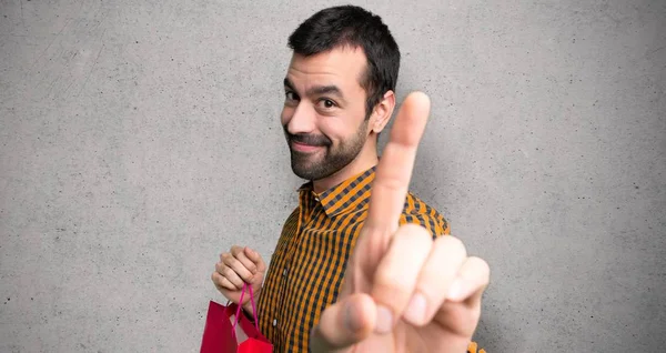 Hombre Con Bolsas Compras Mostrando Levantando Dedo Sobre Pared Texturizada —  Fotos de Stock