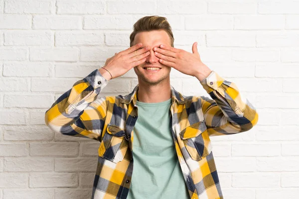 Blonďatý Pohledný Muž Přes Bílou Cihlovou Zeď Zakrývající Oči Rukama — Stock fotografie