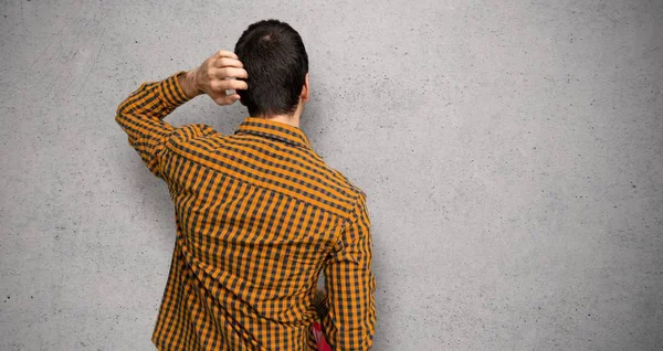 Man with shopping bags on back position looking back while scratching head over textured wall