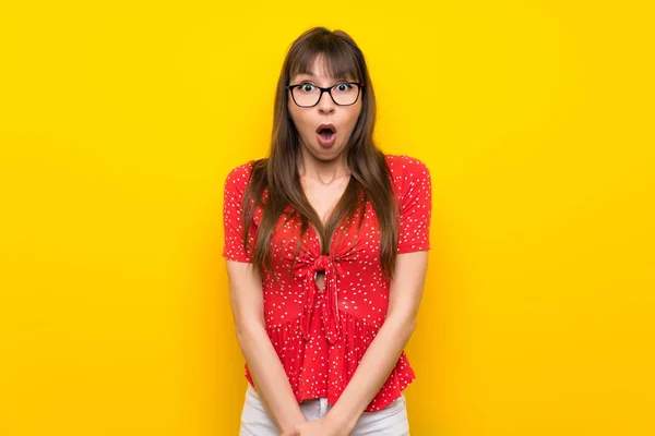 Young woman over yellow wall with surprise facial expression