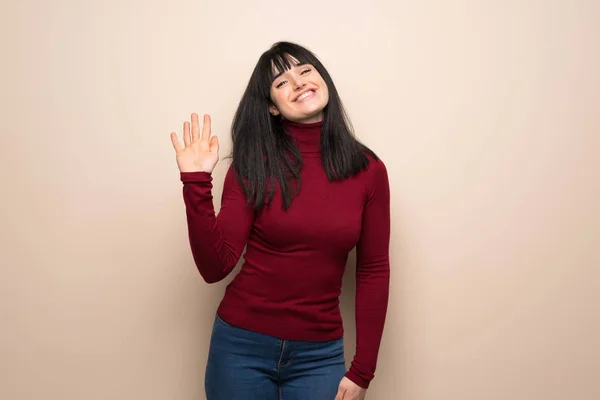 Young woman with red turtleneck saluting with hand with happy expression