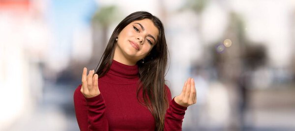 Teenager girl with turtleneck making money gesture at outdoors