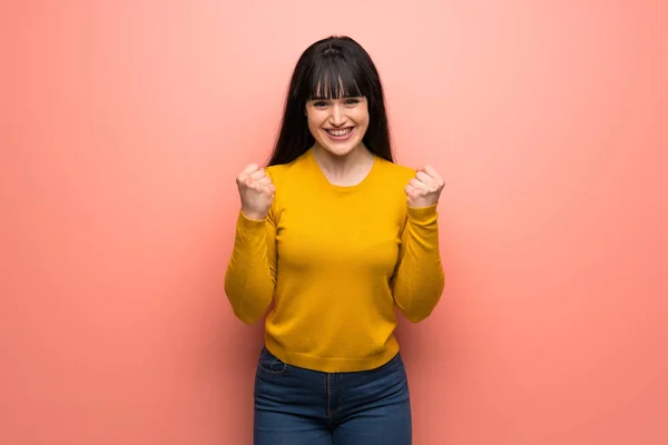 身穿黄色毛衣的女子翻过粉红墙庆祝胜利 — 图库照片