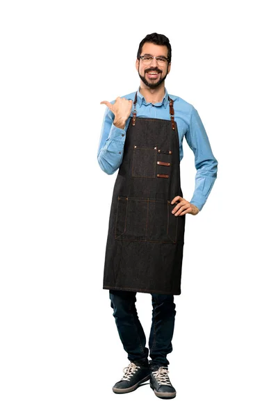 Full-length shot of Man with apron pointing to the side to present a product over isolated white background