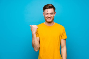 Bir ürün sunmak için yan işaret mavi duvar üzerinde Redhead adam