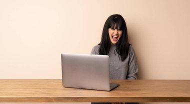 Dizüstü bilgisayarıyla çalışan genç bir kadın ağzı açık bağırıyor.