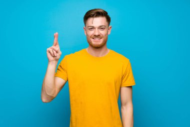 Mavi duvarın üzerinde kızıl saçlı adam parmaklarını geçiyor ve en iyisini dileyerek