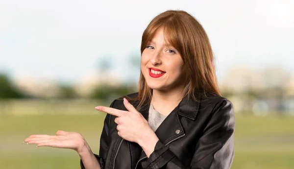 屋外で広告を挿入するために手のひらに架空の Copyspace を保持している若い赤毛の女性 — ストック写真