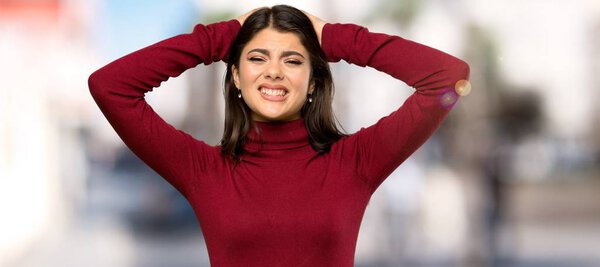 Teenager girl with turtleneck frustrated and takes hands on head at outdoors