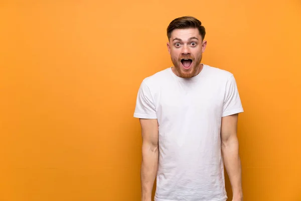 Redhead man over brown wall with surprise facial expression