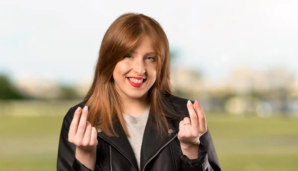 屋外でお金のジェスチャーを作る若い赤毛の女性 — ストック写真