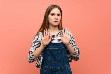 Pembe duvarda tulumlu genç bir kadın iki eliyle dur işareti yapıyor.