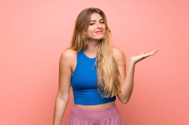 İzole edilmiş pembe arka planı olan genç sarışın kadın bir ilan vermek için avucunda hayali bir fotokopi makinesi tutuyor.