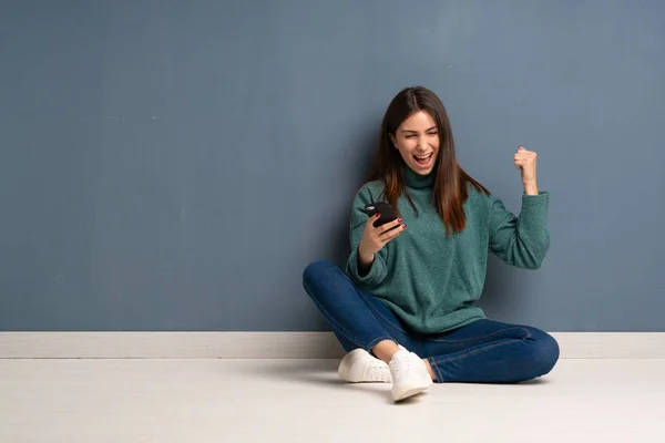 Junge Frau Sitzt Mit Handy Siegerpose Auf Dem Boden — Stockfoto