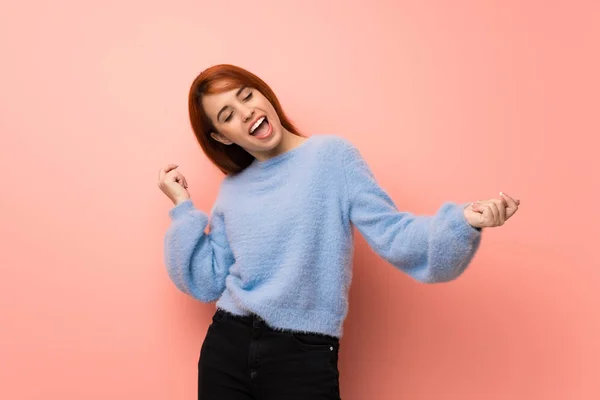 Young redhead woman over pink background enjoy dancing while listening to music at a party