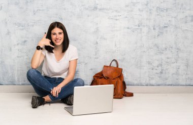 Öğrenci kadın yerde oturmuş telefon hareketi yapıyor. Beni geri arayın işareti