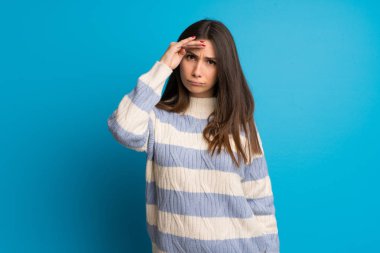 Mavi duvarın arkasında genç bir kadın var. Bir şeye bakmak için çok uzaklara bakıyor.