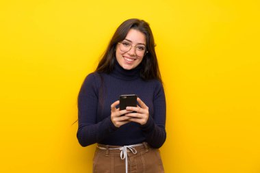 Cep telefonu ile bir mesaj göndererek izole sarı duvar üzerinde Genç kız