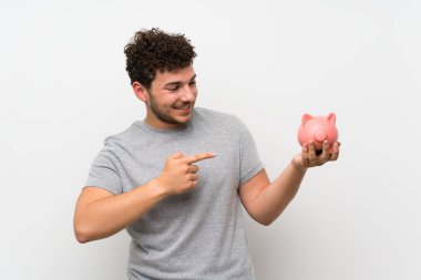 Büyük bir kumbara tutan izole duvar üzerinde kıvırcık saçlı adam