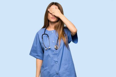 Genç hemşire elleriyle gözlerini kapatıyor. İzole edilmiş mavi arkaplanda bir şey görmek istemezsiniz