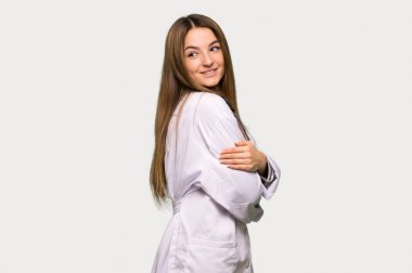 Young doctor woman looking over the shoulder with a smile on isolated grey background