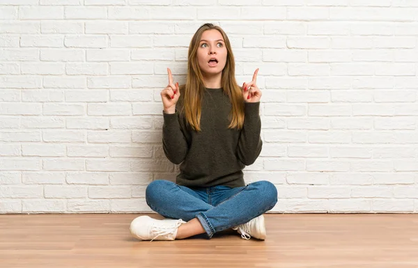 Młoda Kobieta Siedząca Podłodze Zaskoczona Wskazująca — Zdjęcie stockowe