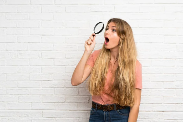 Mladá Blondýna Žena Přes Bílou Cihlovou Zeď Drží Lupu — Stock fotografie