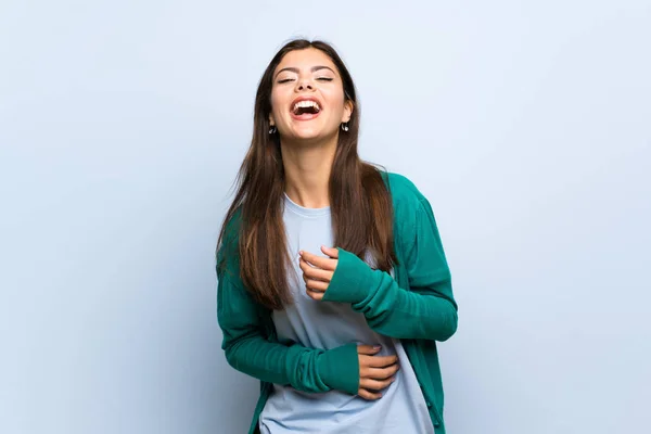 Teenager girl over blue wall smiling a lot