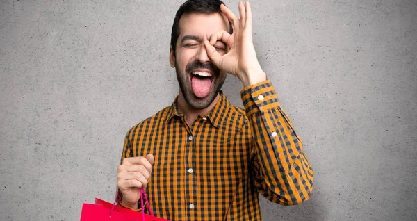 Man with shopping bags makes funny and crazy face emotion over textured wall