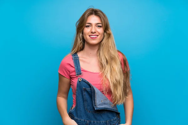 Genç Sarışın Kadın Mavi Duvardan Sarkık Tulumuyla Gülüyor — Stok fotoğraf